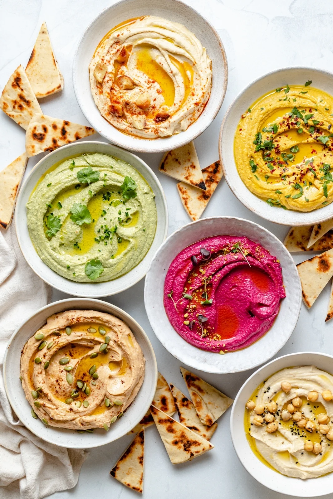 Bowls of Cool Specialty Foods hummus arranged on white marble.